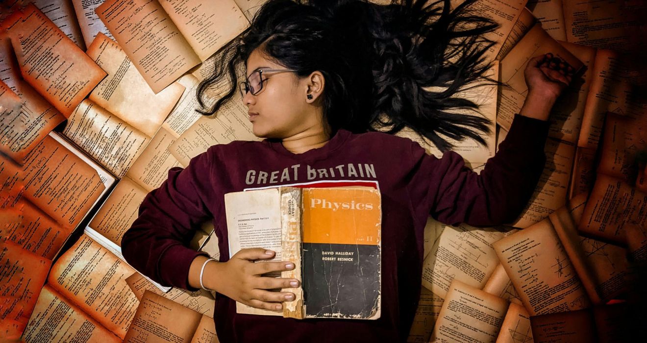 Exams. Girl lying on a pile of books.